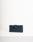 Natural-grained unlined wallet. It features a front snap closure, 8 card slots, 2 bill compartments plus a zippered interior pocket.