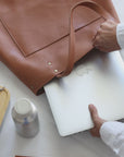 Leather Tote Bag
Full grain leather, unlined hand bag. It features two open exterior pockets and one internal zippered pocket. It comes with fixed leather handles. It’s held shut by a sturdy snap closure.