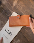 Natural-grained unlined wallet. It features a front snap closure, 8 card slots, 2 bill compartments plus a zippered interior pocket.