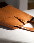 Leather Tote Bag
Full grain leather, unlined hand bag. It features two open exterior pockets and one internal zippered pocket. It comes with fixed leather handles. It’s held shut by a sturdy snap closure.