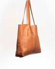 Leather Tote Bag, unlined hand bag. It features two open exterior pockets and one internal zippered pocket. It comes with fixed leather handles. It’s held shut by a sturdy snap closure.