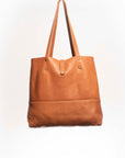 Leather Tote Bag, unlined hand bag. It features two open exterior pockets and one internal zippered pocket. It comes with fixed leather handles. It’s held shut by a sturdy snap closure.