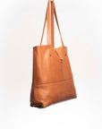 Leather Tote Bag
Full grain leather, unlined hand bag. It features two open exterior pockets and one internal zippered pocket. It comes with fixed leather handles. It’s held shut by a sturdy snap closure.