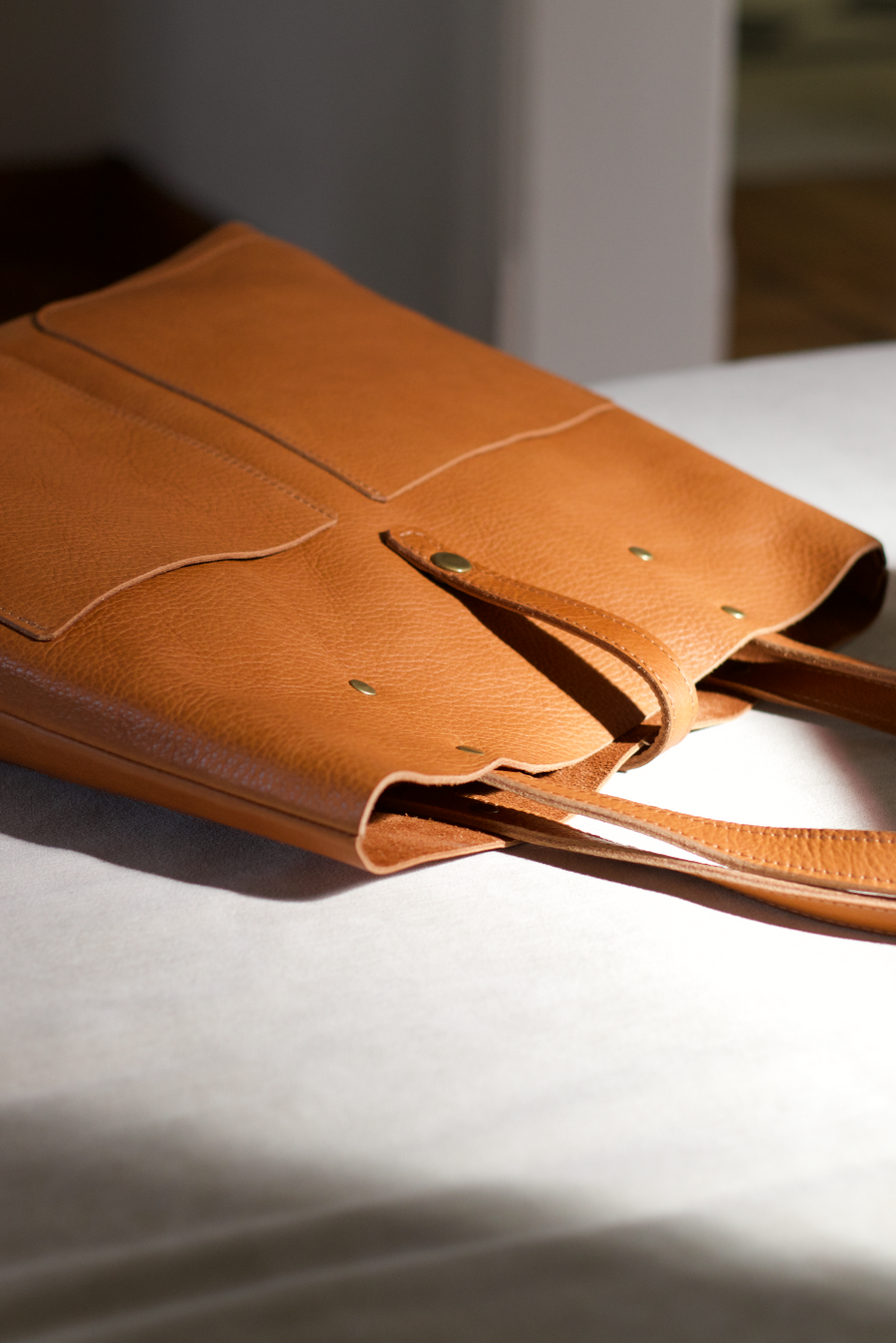 Leather Tote Bag
Full grain leather, unlined hand bag. It features two open exterior pockets and one internal zippered pocket. It comes with fixed leather handles. It’s held shut by a sturdy snap closure.