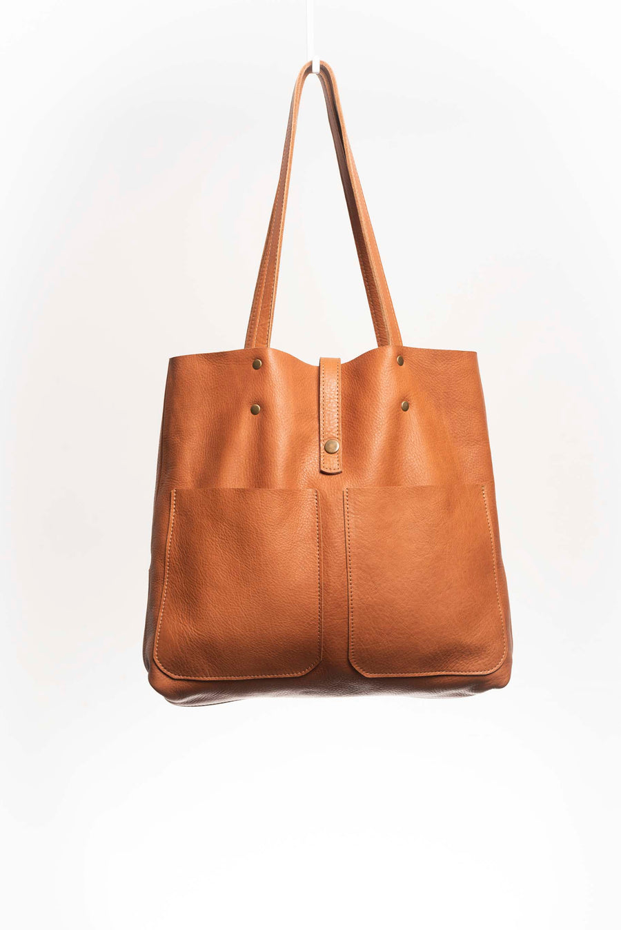 Leather Tote Bag
Full grain leather, unlined hand bag. It features two open exterior pockets and one internal zippered pocket. It comes with fixed leather handles. It’s held shut by a sturdy snap closure.