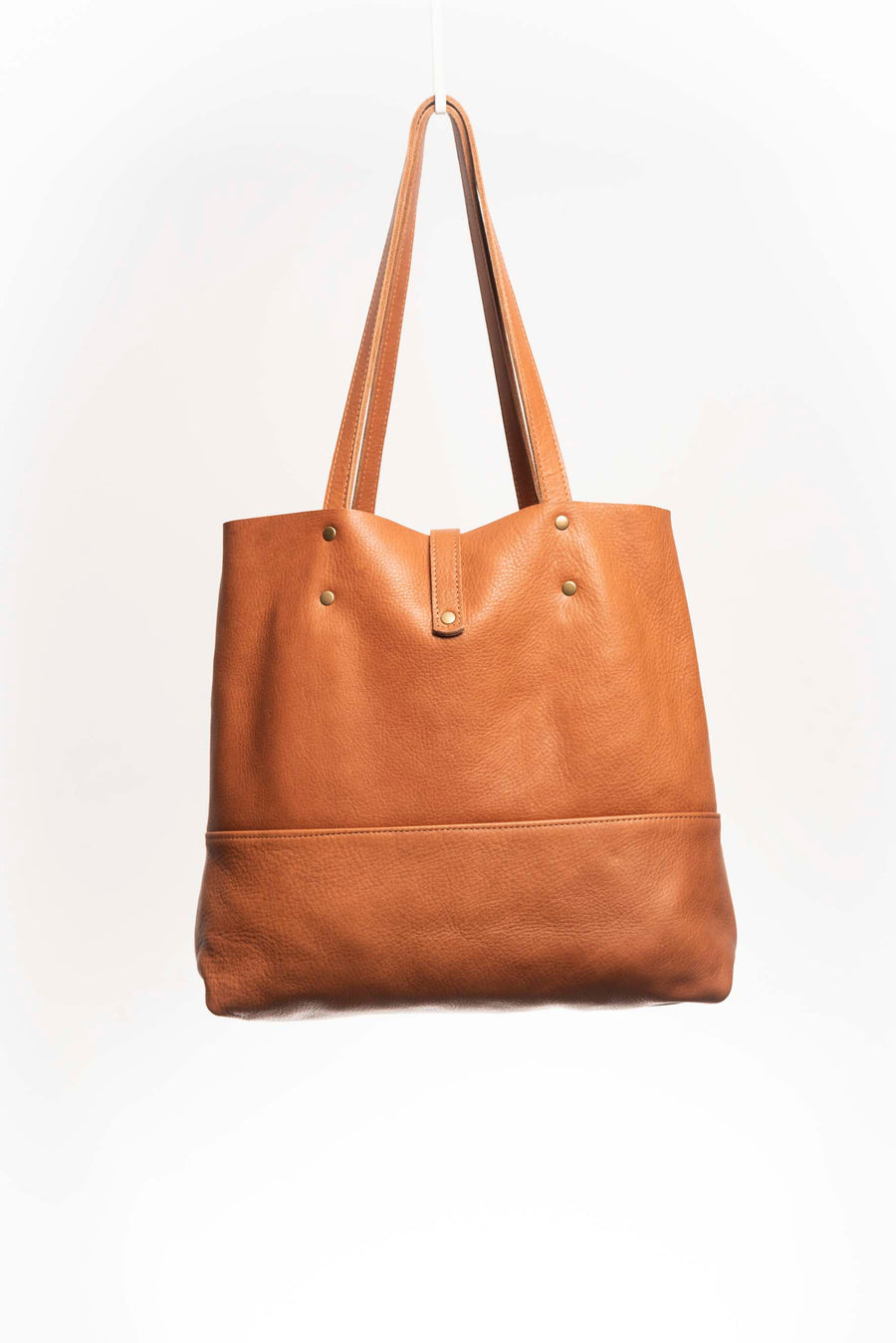 Leather Tote Bag, unlined hand bag. It features two open exterior pockets and one internal zippered pocket. It comes with fixed leather handles. It’s held shut by a sturdy snap closure.
